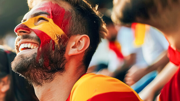 Ein spanischer Fußball-Fan hat das Gesicht mit den Farben der Landesflagge bemalt und lacht 